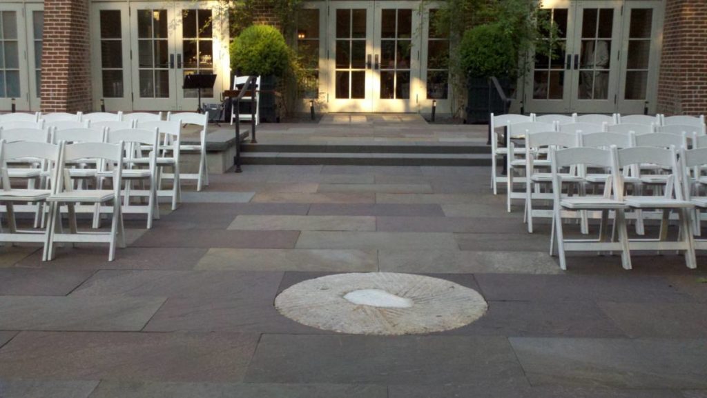 A stone patio with folding chairs on either side of an aisle. The chairs face away from stone porch accessible by going up 2 steps.