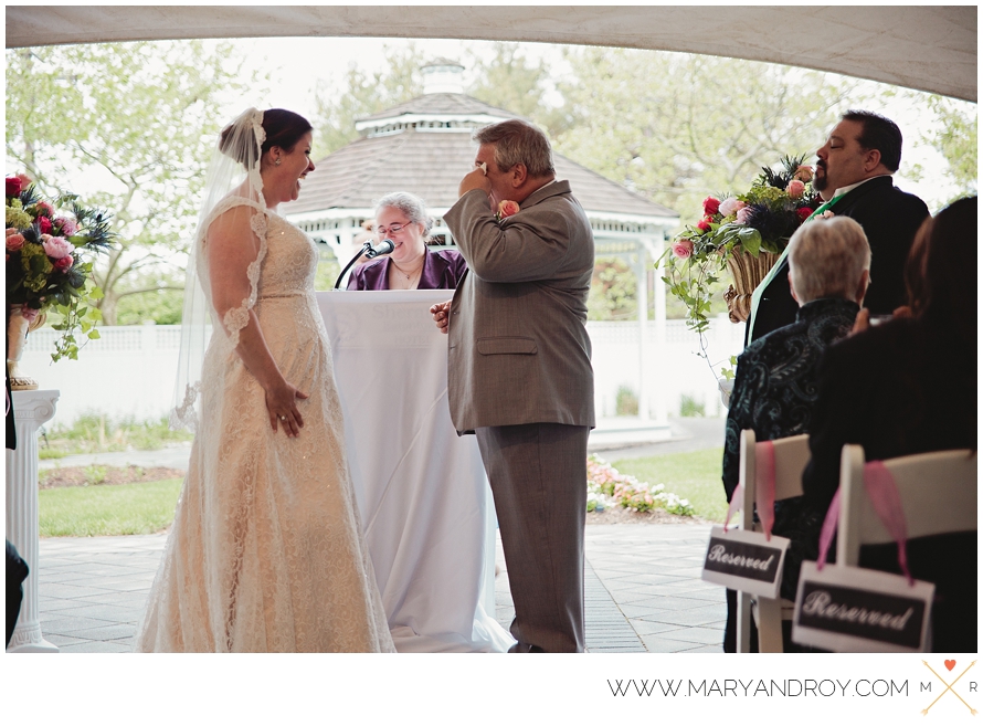 On a crisp spring day, groom Johnnie wipes a tear from his eye and bride Megan smiles as they listen to officiant Cris tell their love story.