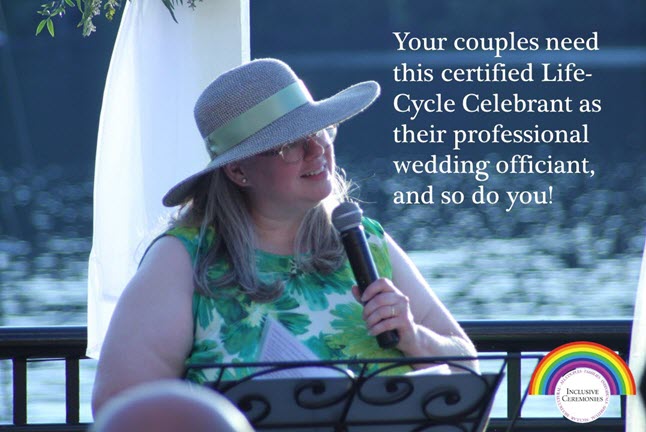 Photo of a wedding officiant. She's wearing a green dress and a wide-brimmed hat with a green ribbon. She's outside, at a podium, holding a microphone. In the background the rippling water of a river sparkles in the sunlight.